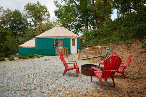 a green yurt sits behind a circle of red adirondack chairs circling a fire pit